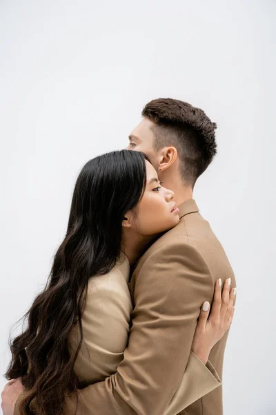 stock image side view of brunette asian woman with long hair embracing stylish man isolated on grey