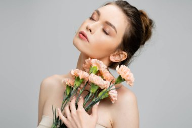 sensual woman with naked shoulders and closed eyes posing with bouquet of carnations isolated on grey