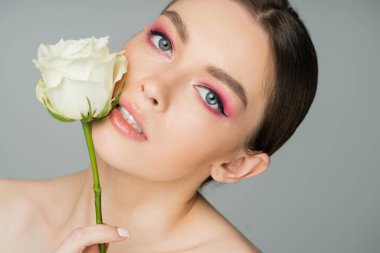 portrait of charming woman posing with white rose near perfect face isolated on grey