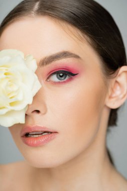 close up portrait of young woman with pink visage obscuring face with ivory rose isolated on grey