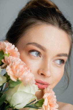 Portrait of pretty young woman looking away near flowers isolated on grey 