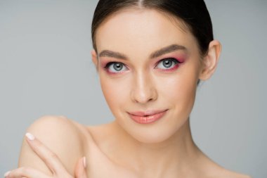 Gülümseyen, makyajlı, çıplak omuzlu bir model. 