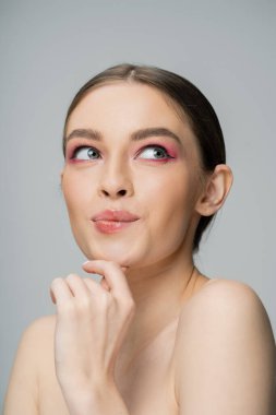Dreamy woman with pink eye shadow and naked shoulders looking up isolated on grey  clipart