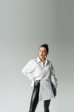Stylish freelancer in shirt and leather pants holding laptop isolated on grey 