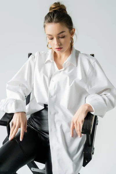 stock image stylish woman sitting on chair in white oversize shirt isolated on grey