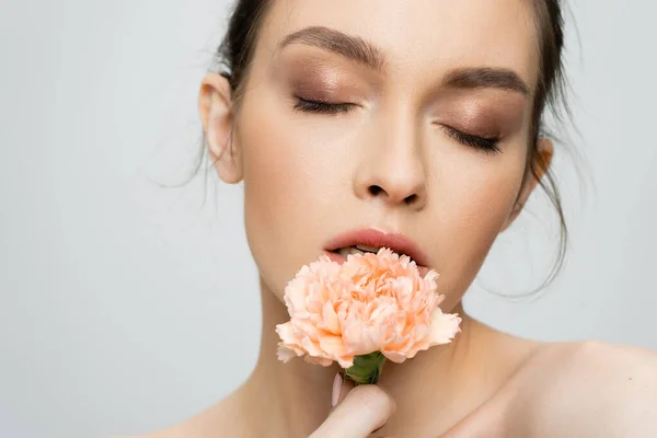 stock image young woman with makeup and closed eyes holding peach carnation near face isolated on grey