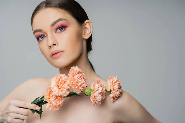 stock image young woman with makeup and bare shoulders posing with fresh flowers and looking at camera isolated on grey