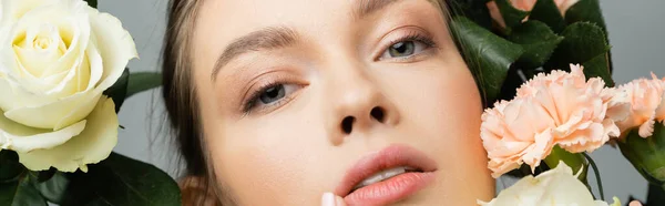 stock image close up portrait of pretty woman with natural makeup looking at camera near flowers isolated on grey, banner