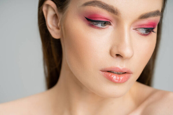 Close up view of young woman with pink eye shadows posing isolated on grey 
