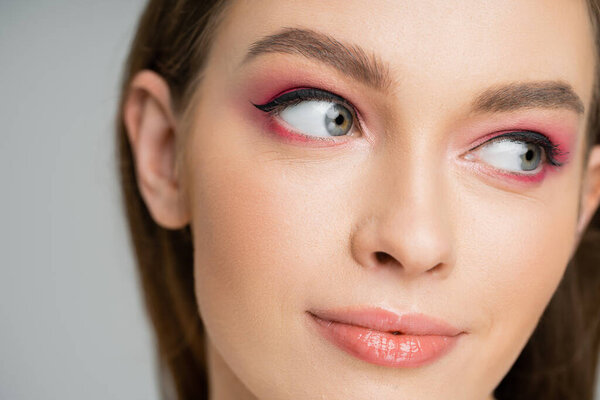 Close up view of young fair haired woman with pink eye shadow isolated on grey 