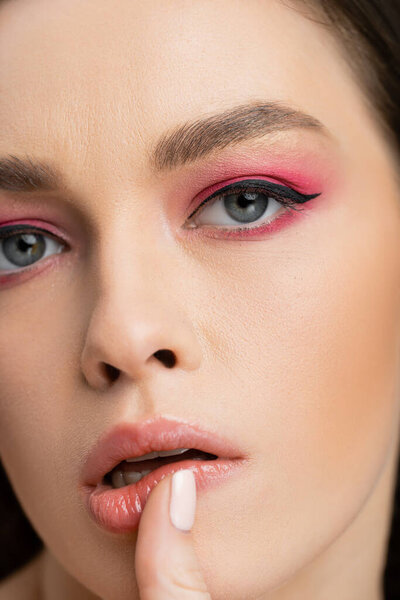 Close up view of young woman with bright eye shadow touching lip isolated on grey 