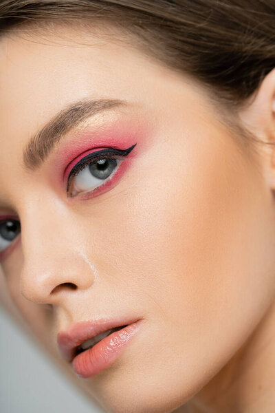 Cropped view of woman with pink eye shadow and eye liner looking at camera isolated on grey 