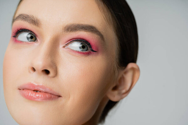 Close up view of woman with pink eye shadow and eye liner isolated on grey 