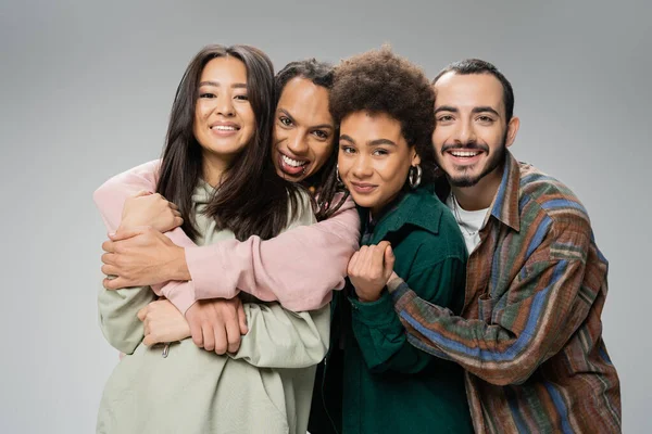 stock image joyful multicultural friends in trendy outfit embracing and looking at camera isolated on grey