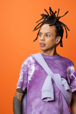 stylish multiracial man in tie-dye t-shirt looking away isolated on orange