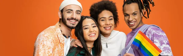 stock image trendy multiracial friends smiling at camera near lgbt flag isolated on orange, banner