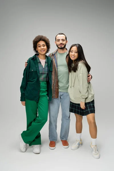 stock image full length of young bearded man embracing happy multiethnic women on grey background