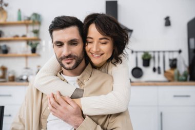 Smiling woman hugging brunette husband at home 