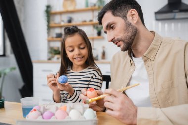 father and happy daughter coloring Easter eggs in kitchen   clipart