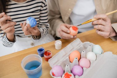 Cropped view of girl and dad coloring Easter eggs at home  clipart