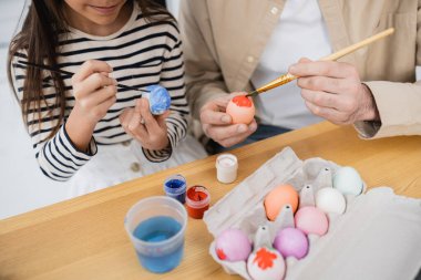 Cropped view of father and daughter coloring Easter eggs at home  clipart