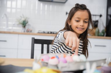 Smiling kid touching blurred Easter egg at home 