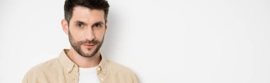 Brunette and bearded man looking at camera on white background, banner 