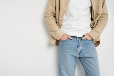 Gömlekli bir adamın beyaz arka planda kot pantolon ceplerinde el ele tutuşması. 