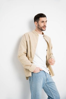 Brunette and bearded man posing in shirt and jeans on white background 