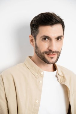 Portrait of brunette man in beige shirt looking at camera on white background 
