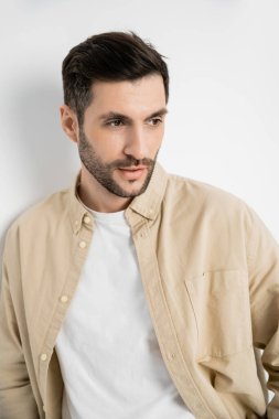Portrait of bearded man in beige shirt looking away on white background 