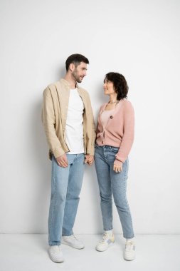 Full length of smiling couple holding hands while standing on white background 