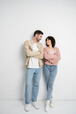 Brunette couple crossing arms while standing on white background 