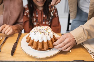Cropped view of man holding knife near Easter cake and family at home 