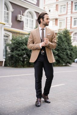 full length of young man in beige formal wear standing on street 