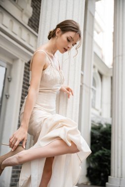 young bride in wedding dress wearing high heeled shoe near house 