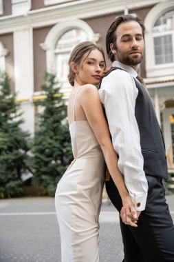 young bride and groom in wedding dress and suit holding hands outside 