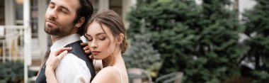 young bride with closed eyes hugging bearded groom in vest, banner 