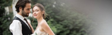 bearded groom in vest embracing happy bride in white dress with wedding bouquet, banner 