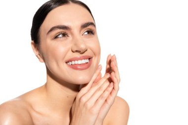 dreamy young woman with bare shoulders and natural makeup looking away while smiling isolated on white 