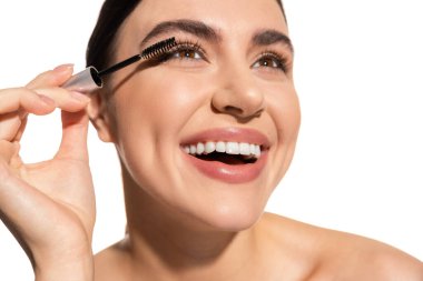 close up of joyful woman applying mascara while looking up isolated on white 