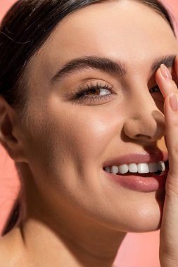 close up view of happy young woman with flawless makeup isolated on pink 