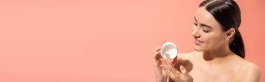 portrait of pleased woman with bare shoulders holding jar with nourishing cream isolated on pink, banner 