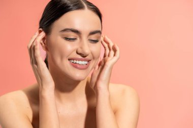 portrait of happy young woman with bare shoulders and flawless makeup smiling isolated on pink 