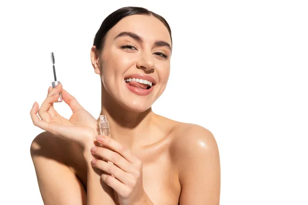 cheerful woman holding eyebrow brush and styling gel while sticking out tongue isolated on white