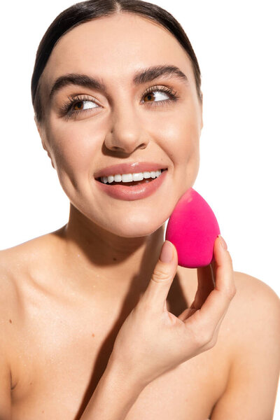 cheerful young woman applying makeup foundation with pink beauty sponge isolated on white 