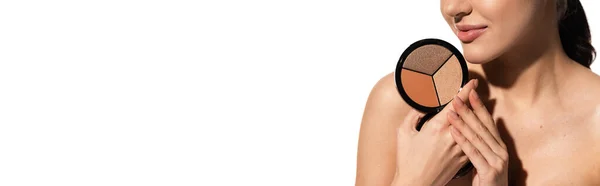 stock image cropped view of young woman with bare shoulder holding bronzer and highlighter palette isolated on white, banner 