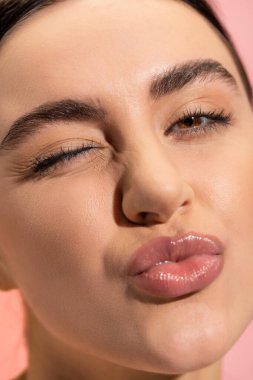 close up of young woman pouting lips and winking eye isolated on pink 