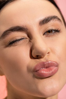 close up of young woman pouting lips and winking eye isolated on pink  clipart