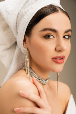 young woman with makeup and towel on head looking at camera on grey background 